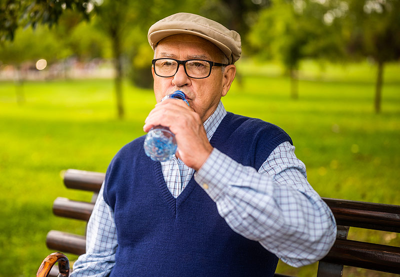 Homme âgé boit de l'eau lors d'une balade à l'extérieur.